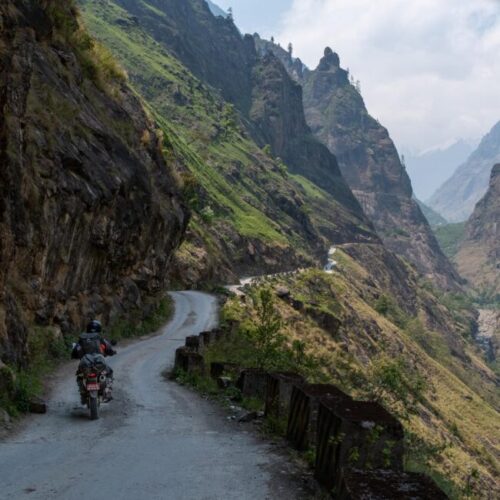 An adventure rider traveling dual-sport motorcycles along scenic mountain road to Chame, Nepal.