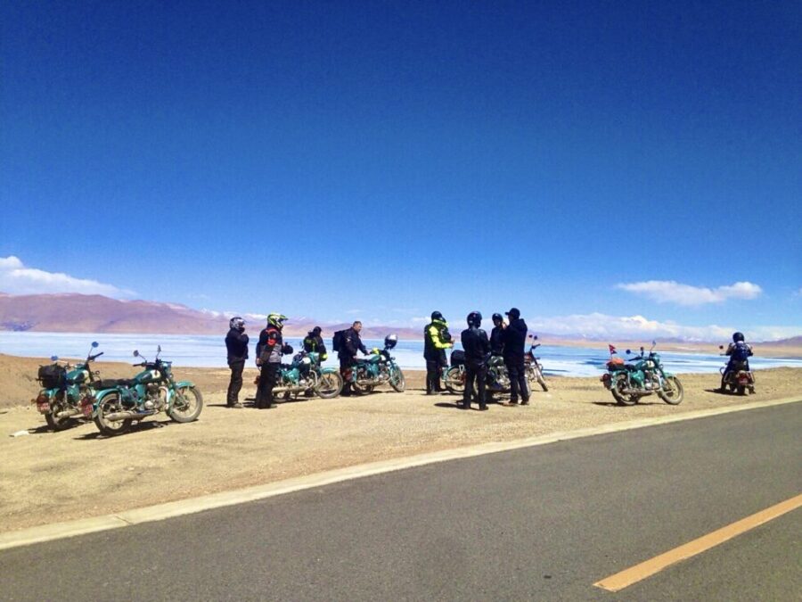 Adventure riders gathering at a scenic pitstop during a guided Bikemandu motorcycle expedition along a rugged mountain road in Nepal.