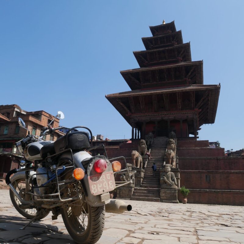 Classic motorcycle parked in historic Bhaktapur Durbar Square on a 5 days Everest Gateway to Chitwan park motorcycle tour route.