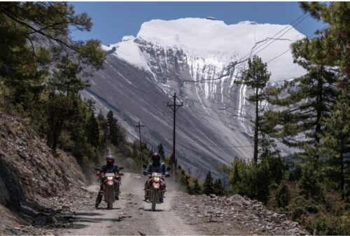 Two dual-sport motorcycle riders journeying to Manang, Nepal, against a majestic Himalayan mountain backdrop on an adventure tour.