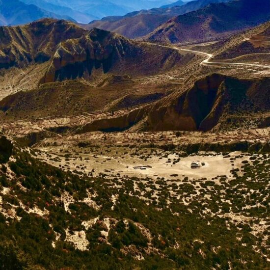Explore the rugged Himalayan desert landscape with barren mountains, winding dirt roads, and dramatic skies on our Upper Mustang motorcycle tour.